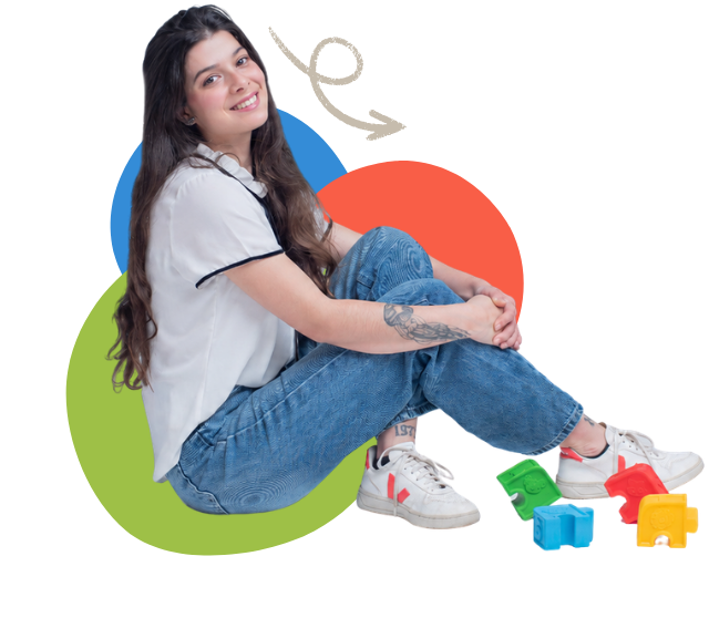 Juliana Meotti sentada no chão, sorrindo, ao lado de blocos de encaixe coloridos usados nas sessões.